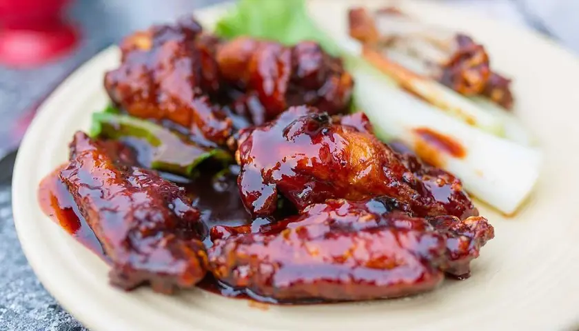 Saftiga kycklingvingar täckta med en glansig, mörk egen barbequesås, serverade med selleristavar och sallad.