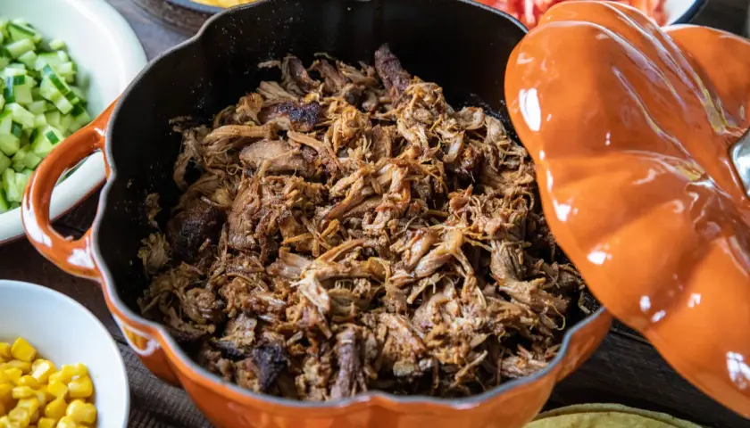 Saftigt pulled pork i en orange gryta, redo för grillen. Serveras med tillbehör som majs, gurka och tomater.