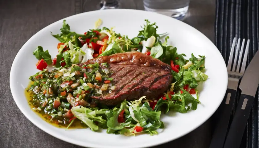 Grillad picanha styckdetalj serverad med en fräsch sallad och chimichurrisås.