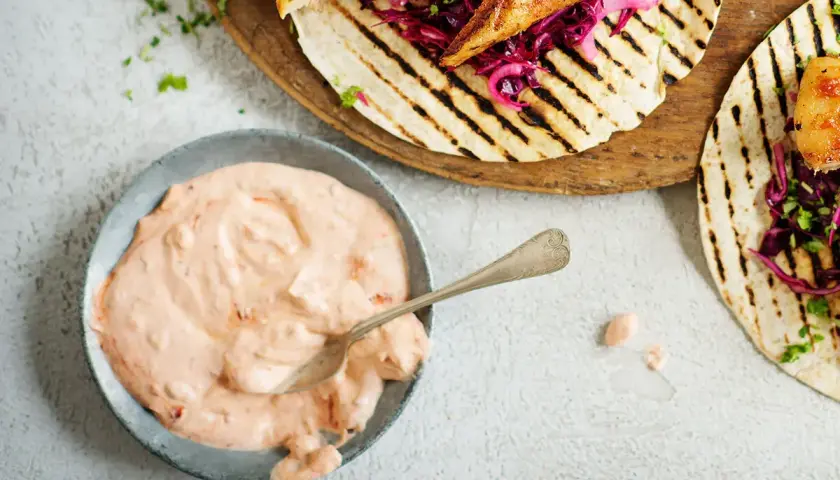 En skål med krämig, rosa hot chilisås bredvid grillade kycklingtacos med rödkål. Perfekt för att addera extra smak!