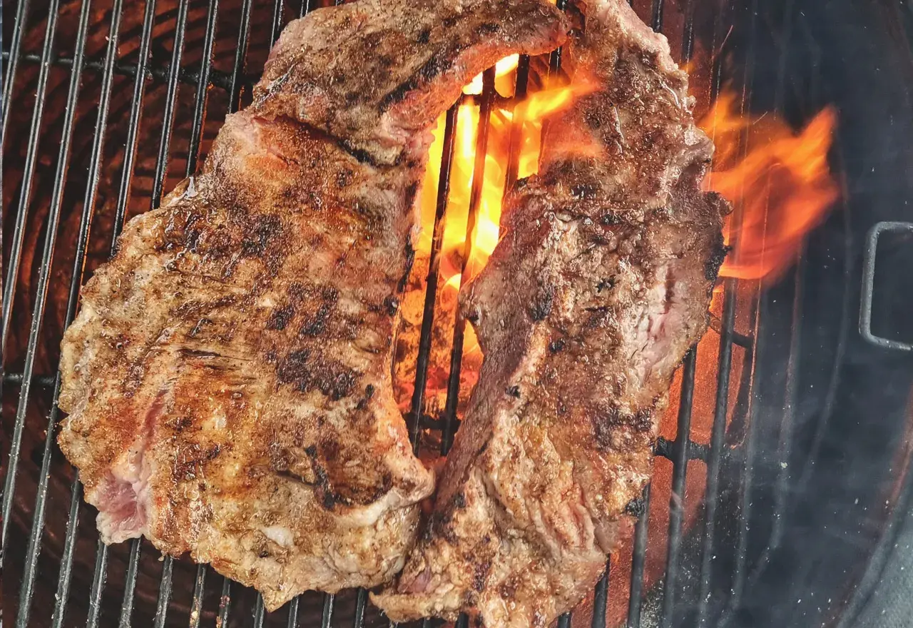 Två saftiga bitar grillad iberico-karré fräser över glödande kol. Flammorna slickar köttet och ger det en perfekt yta.