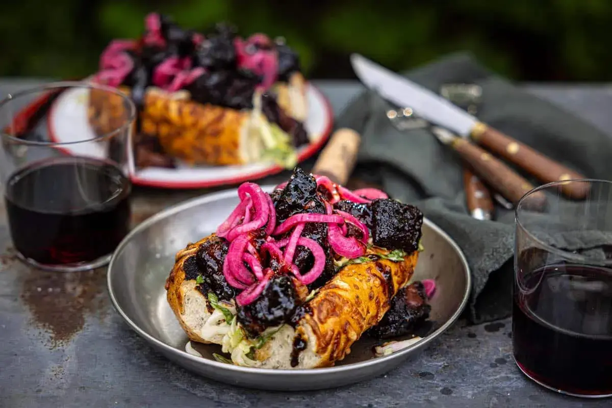 En saftig amerikansk barbeque-smörgås med möra köttbitar och picklad rödlök, serverad med rödvin.