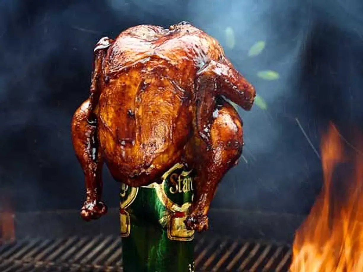 En saftig ölkyckling, perfekt grillad med gyllene skinn, står stolt på en ölburk. Rök och flammor skapar en dramatisk bakgrund.