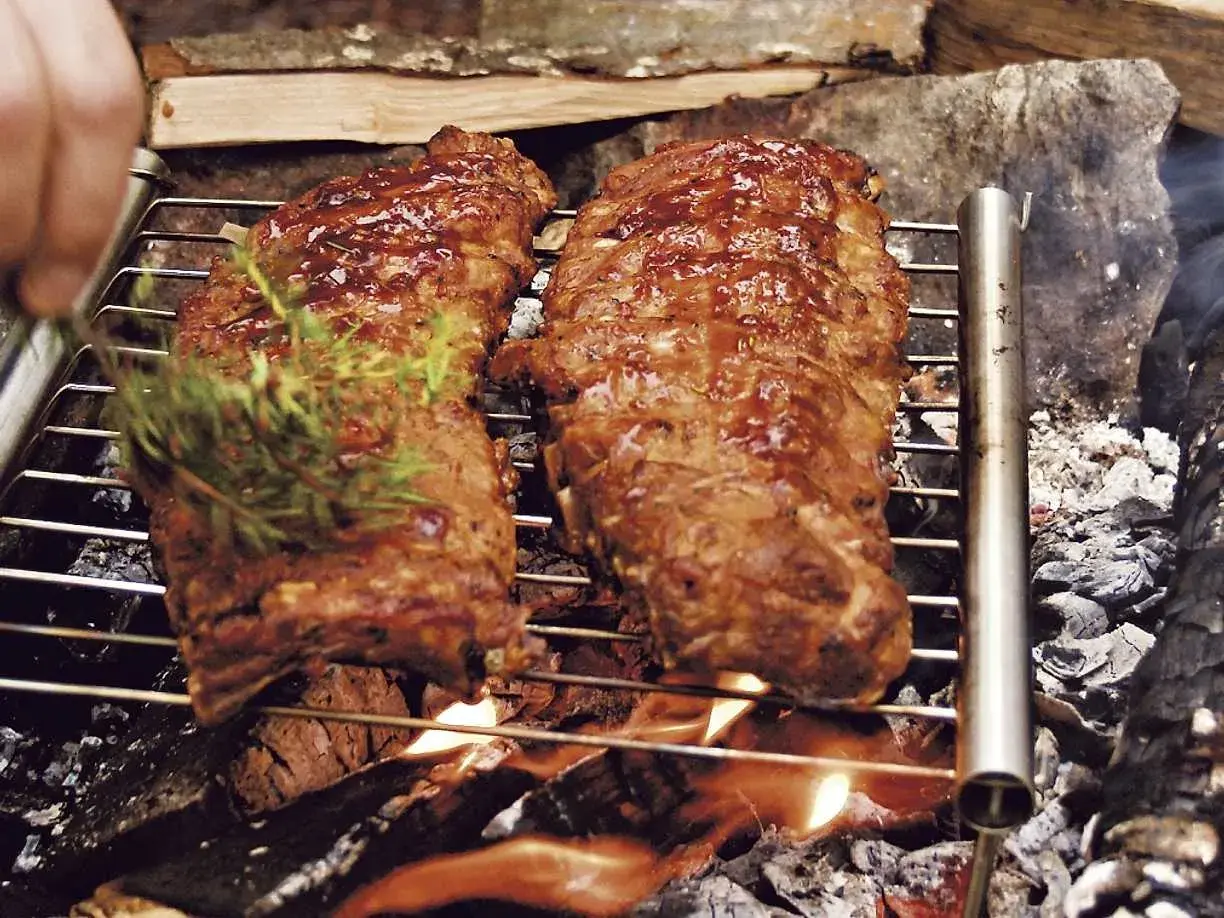 Två saftiga grillade spareribs på ett grillgaller över öppen eld. En kvist rosmarin läggs på för extra smak.