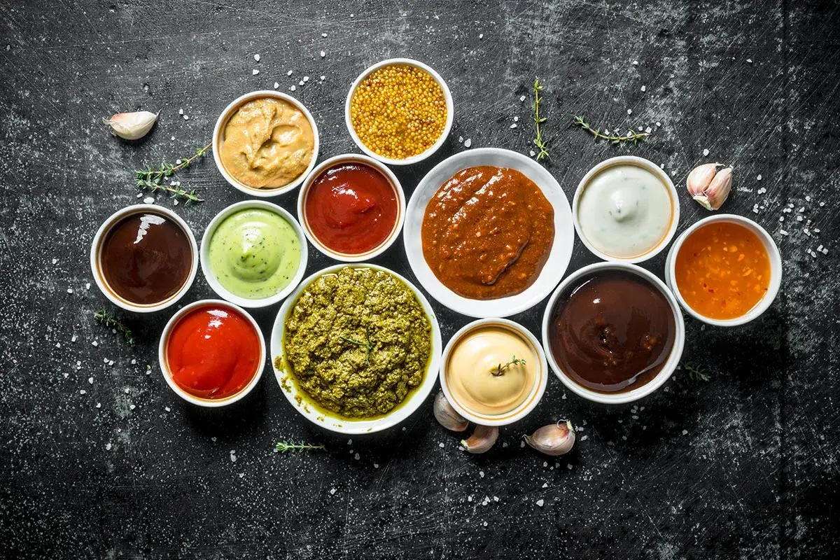 Olika såser i skålar, perfekt för att hitta inspiration till ditt eget barbequesås recept. Här finns allt från röd ketchup till grön pesto.