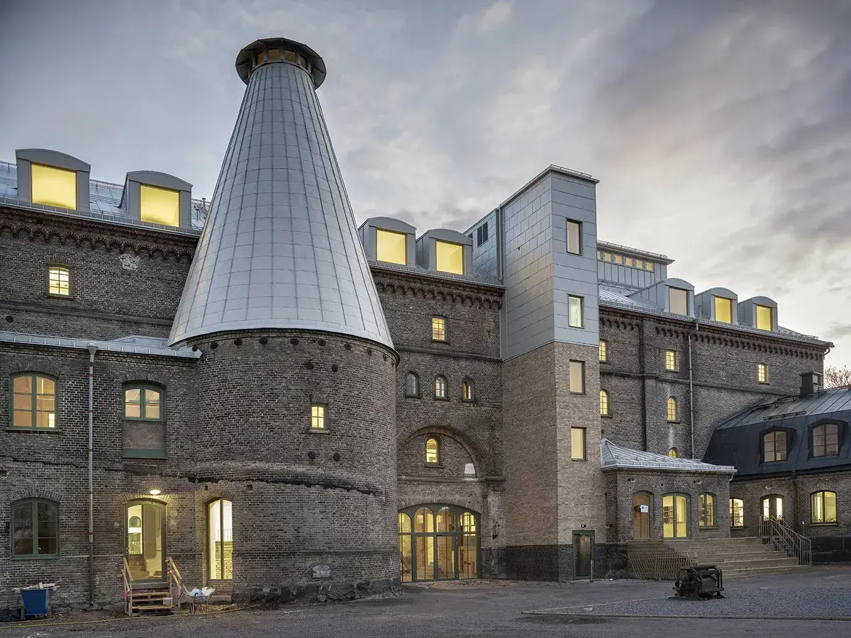 Imponerande tegelbyggnad med ett konformat torn, likt en gigantisk tuva av **panicum virgatum** mot en dramatisk himmel.