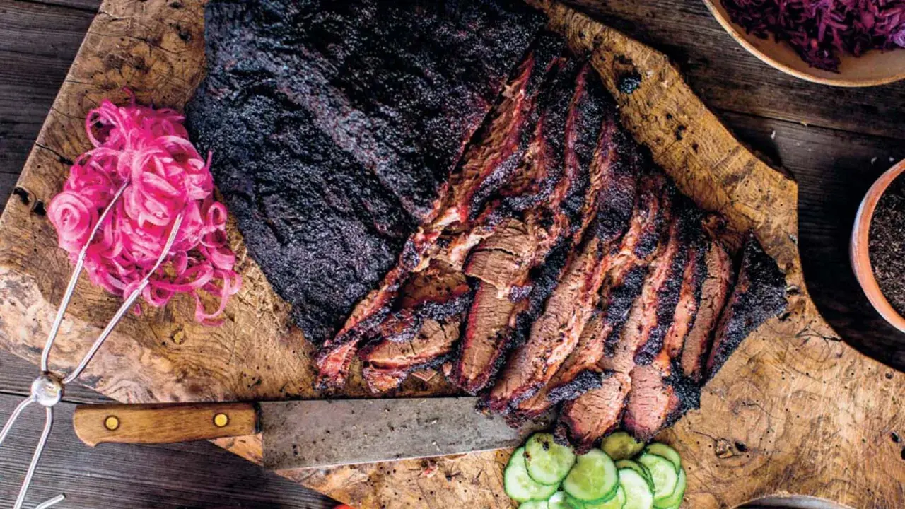 En saftig, grillad brisket skuren i skivor, serverad med picklad rödlök och gurka på en träskärbräda.