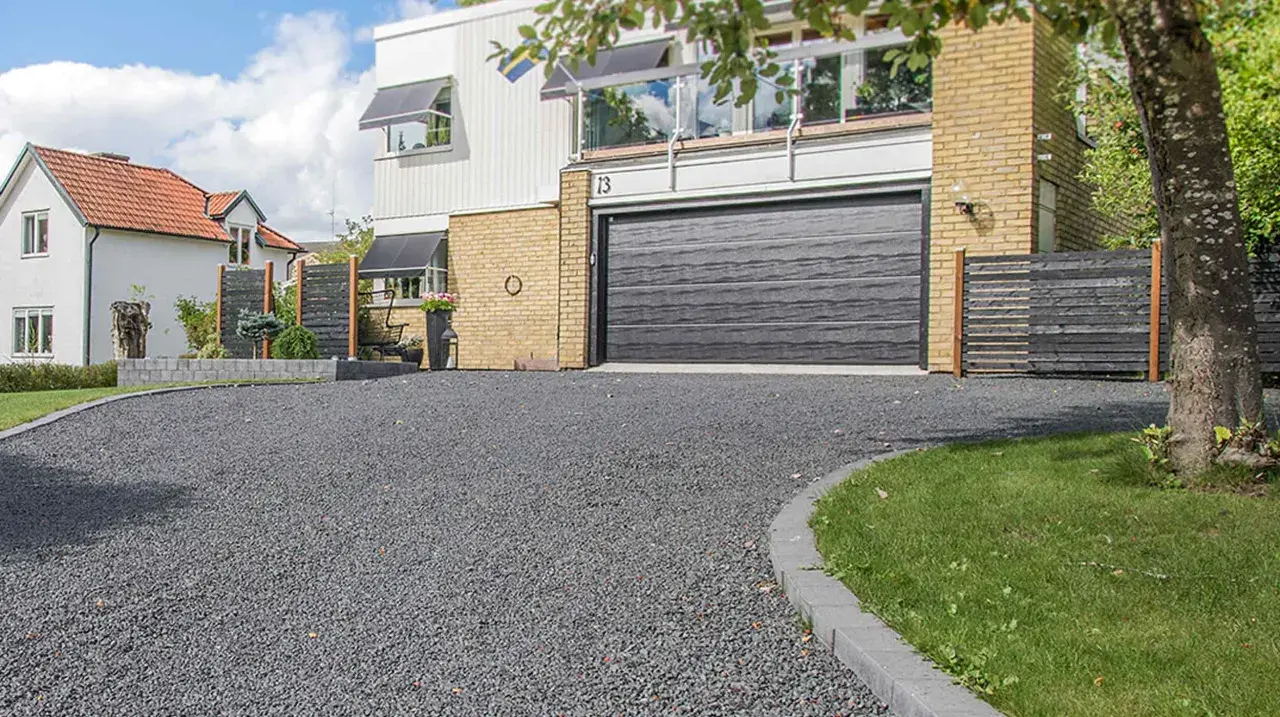 En grå stenlagd uppfart leder fram till ett modernt hus med garageport. Perfekt uppfart inspiration för en stilren entré.