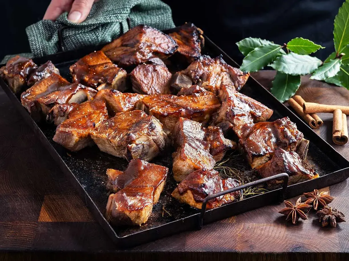 En bricka med saftiga revbensspjäll, täckta av en glansig revbens glaze. Kryddor som kanel och stjärnanis ligger bredvid.