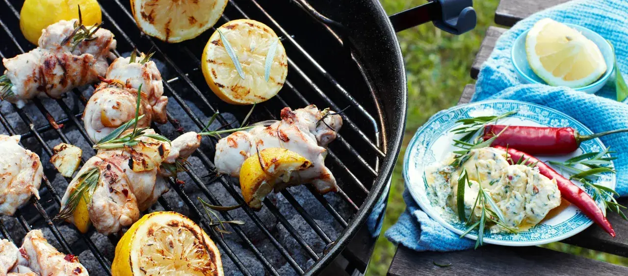 Grillade kycklingklubbor med citron och rosmarin, redo att serveras med en krämig sås och chili.