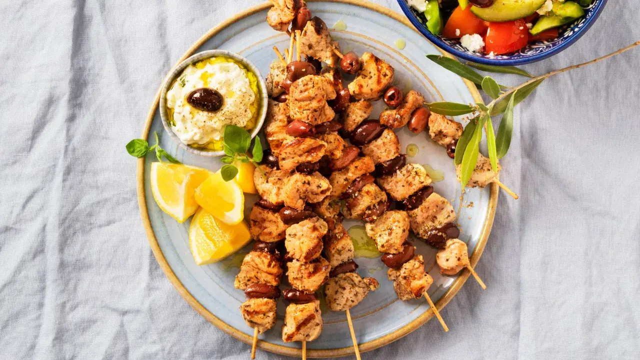 Grillade kycklingspett med oliver, citronklyftor och en krämig dipp. Perfekt för en somrig middag med smak av souvlaki marinad.