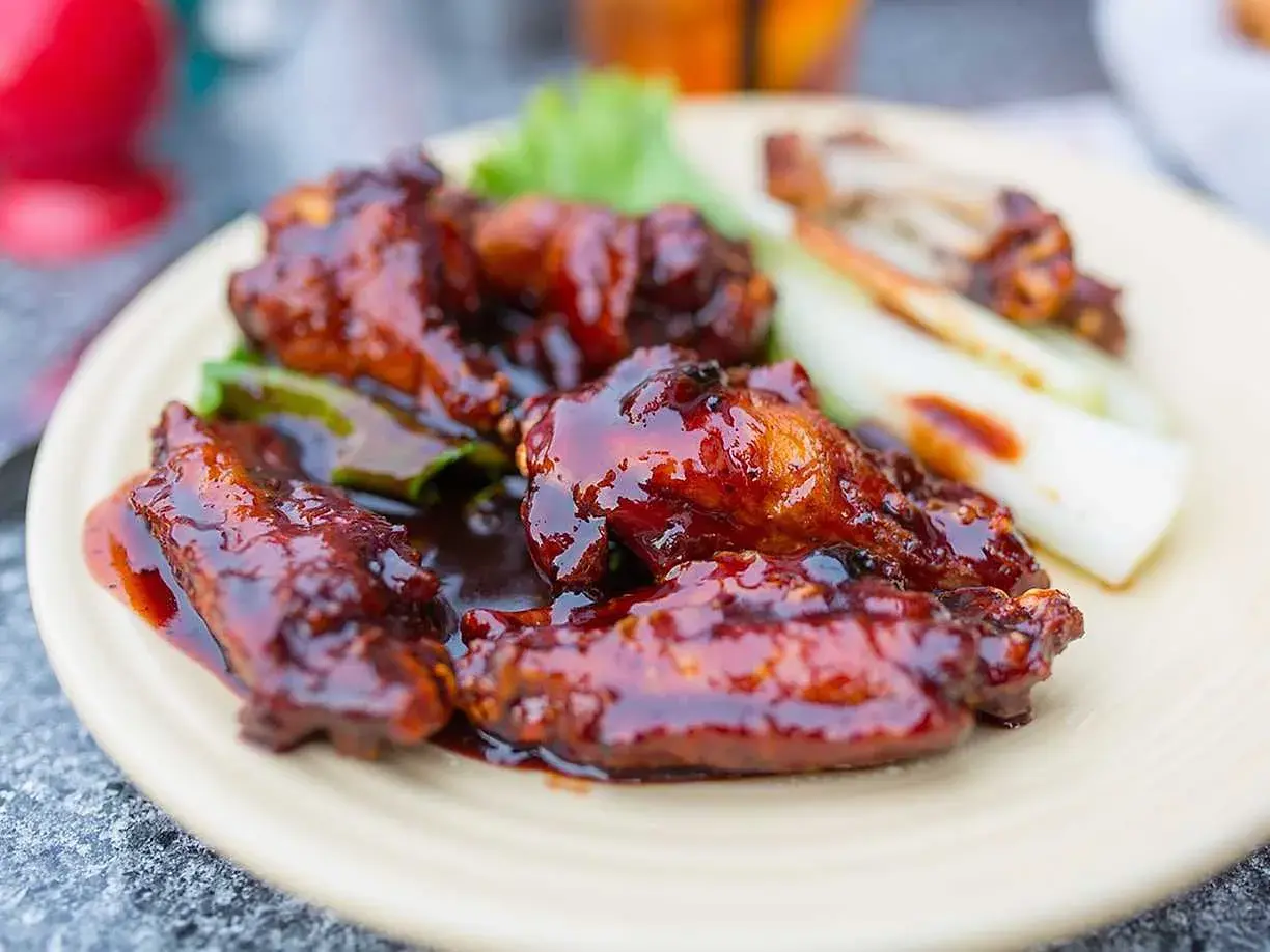 Saftiga kycklingvingar täckta med en glansig, mörk egen barbequesås, serverade med selleristavar och sallad.