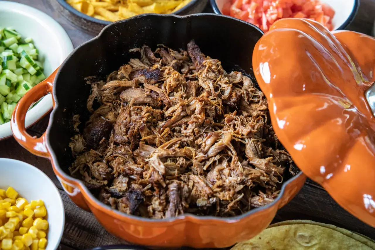 Saftigt pulled pork i en orange gryta, redo för grillen. Serveras med tillbehör som majs, gurka och tomater.