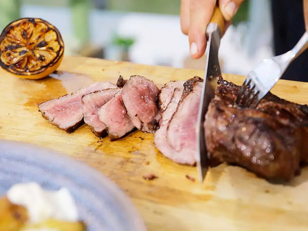 Perfekt grillad ryggbiff skärs upp på en träskärbräda. En grillad citron ligger bredvid.