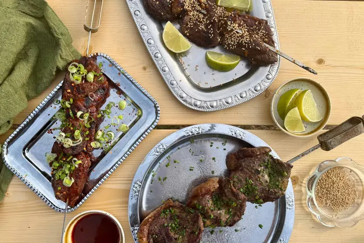 Grillad oxbringa på spett, toppad med salladslök och chiliflakes. Serveras med limeklyftor och sesamfrön.