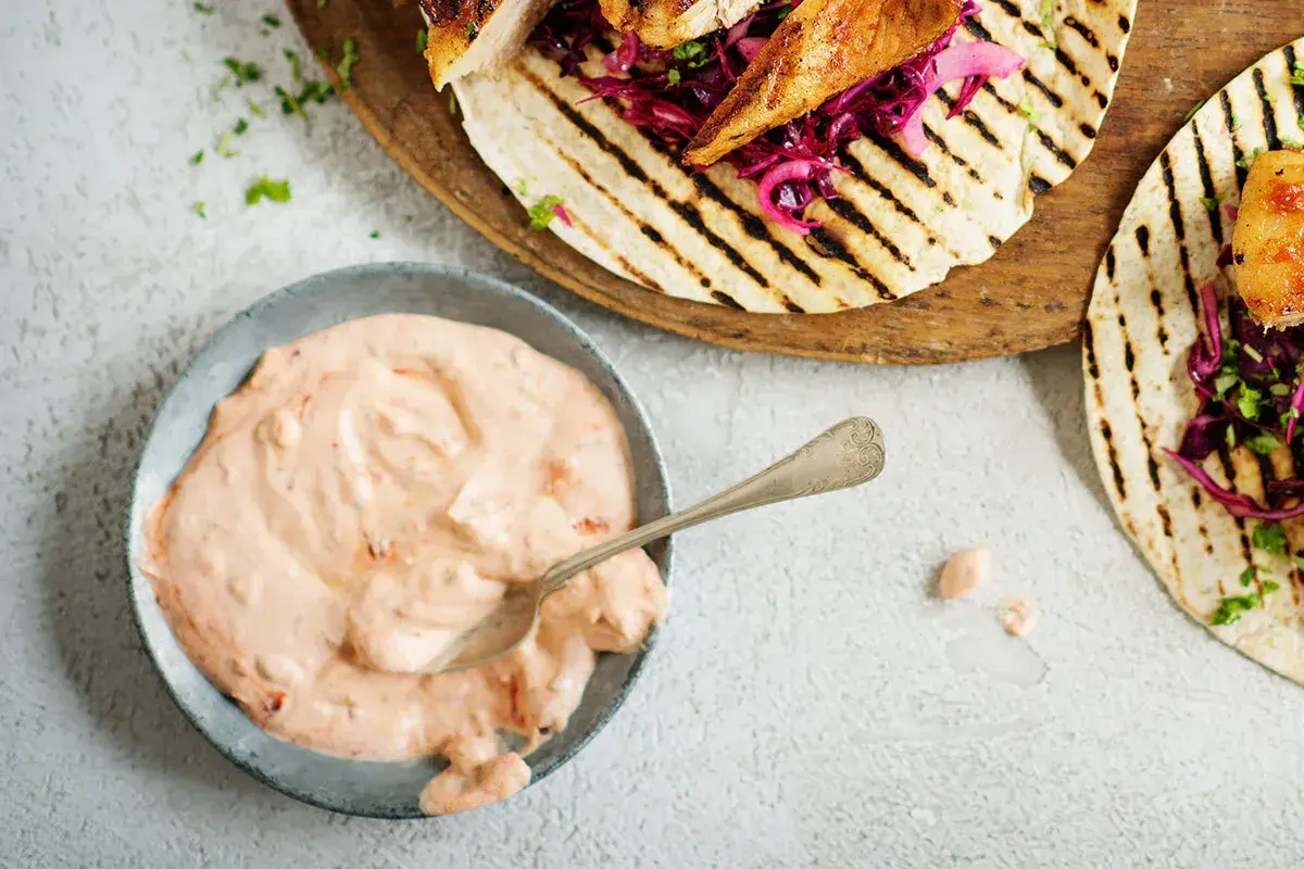 En skål med krämig, rosa hot chilisås bredvid grillade kycklingtacos med rödkål. Perfekt för att addera extra smak!