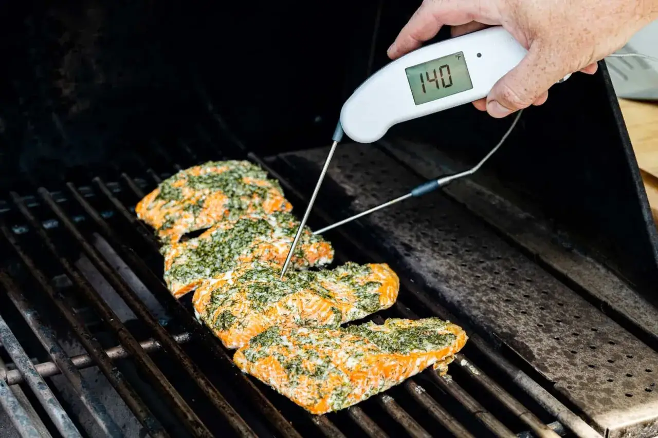 Grillad lax med örtkryddor på grillen, en termometer visar 140°F. Perfekt grillad lax temperatur.