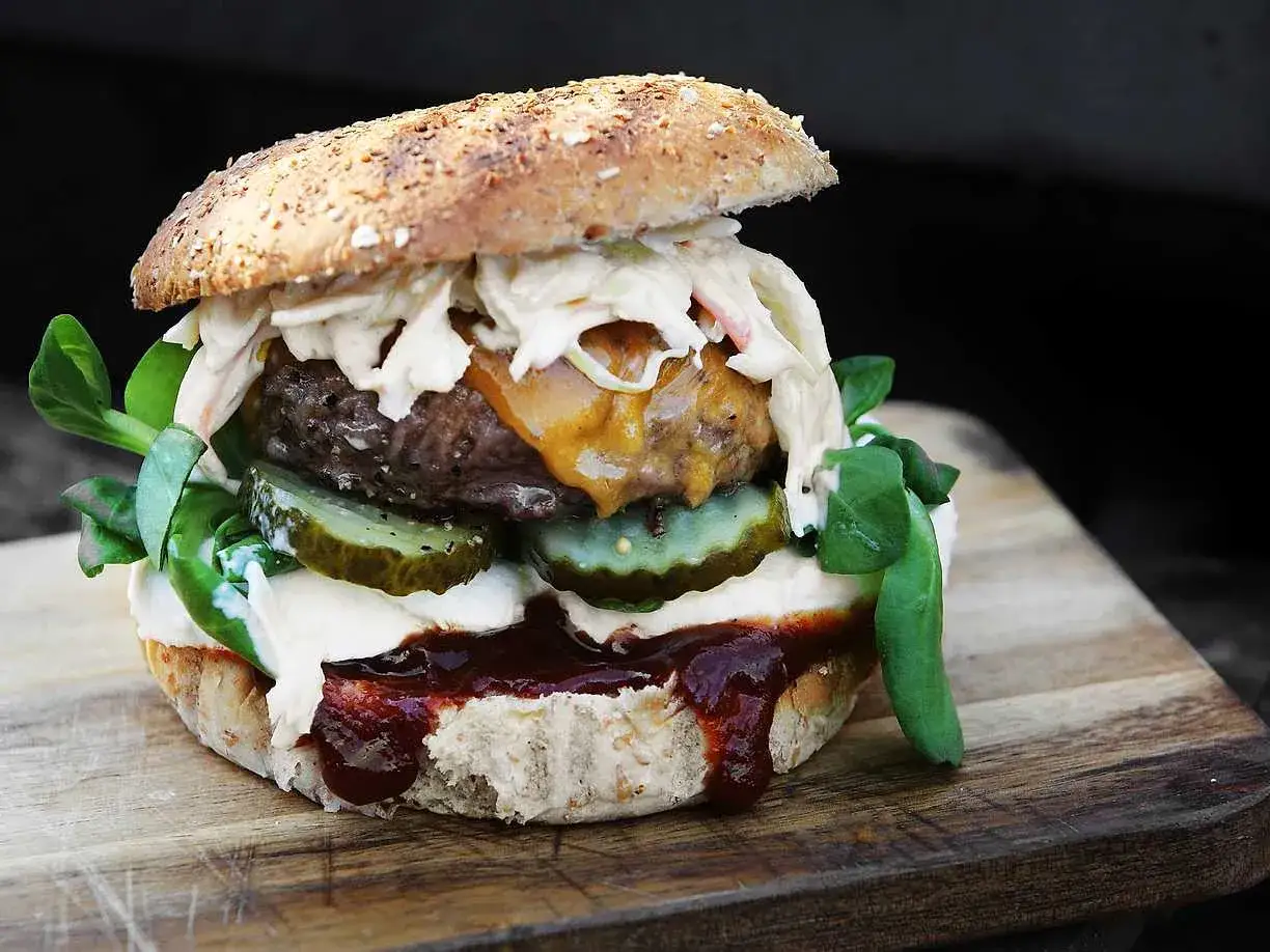En saftig hamburgare med ost, pickles och coleslaw, redo att grilla hamburgare.