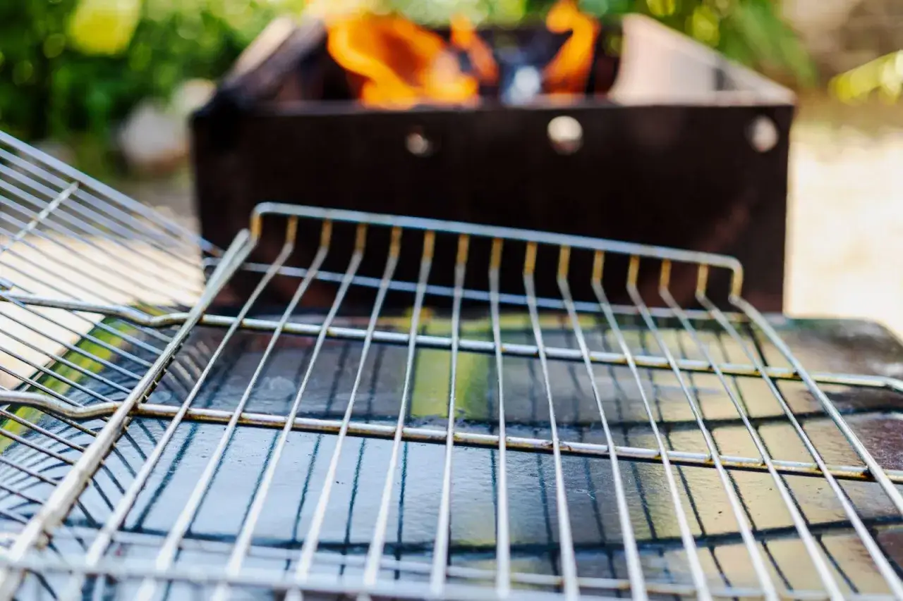 Grillgallret &auml;r redo att oljas in. Flammor syns i bakgrunden fr&aring;n grillen.