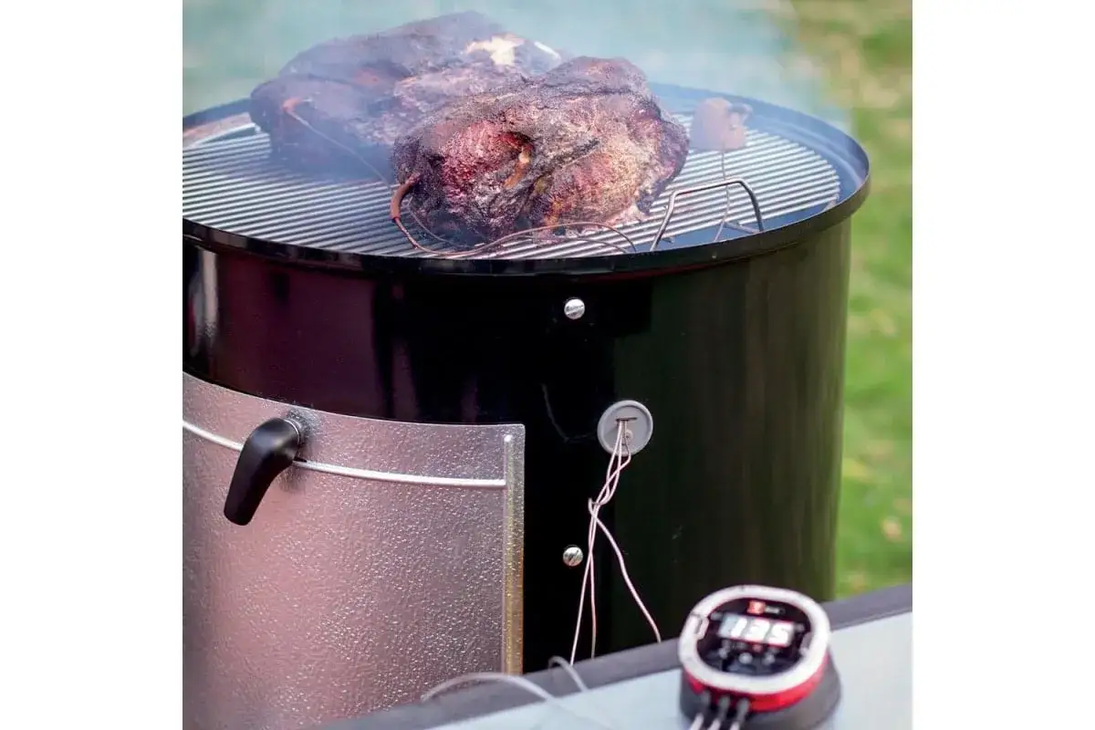 Tv&aring; stora k&ouml;ttbitar ryker p&aring; en grill, redo f&ouml;r amerikansk barbeque. En digital termometer visar temperaturen.