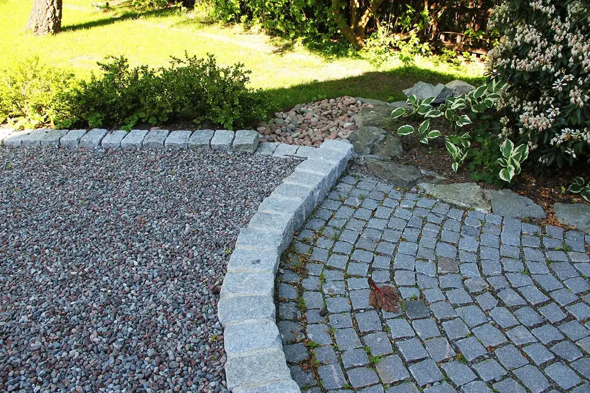 Vacker uppfart inspiration med grus och stenl&auml;ggning, kantad av gr&aring; stenar och omgiven av gr&ouml;nska.