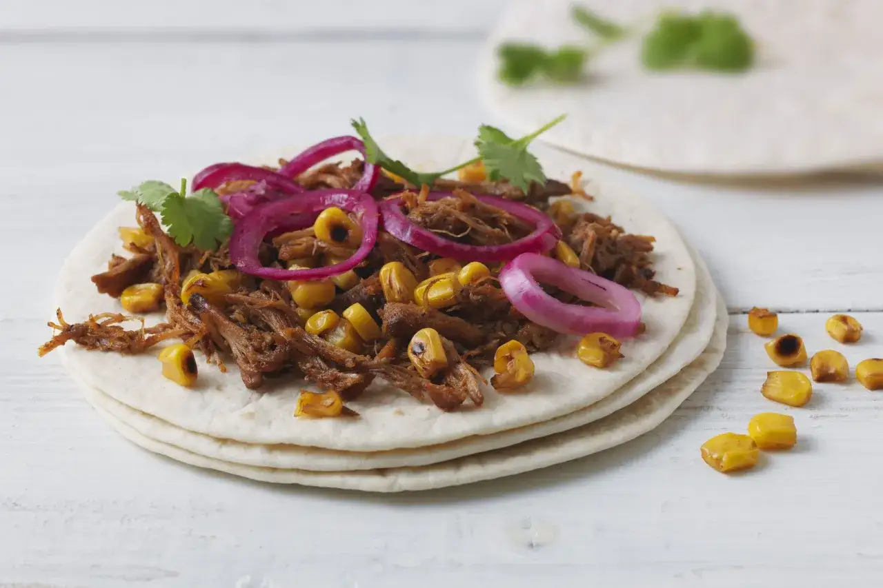 En taco med pulled pork, majs och rödlök. Den här såsen till pulled pork är perfekt för tacos.