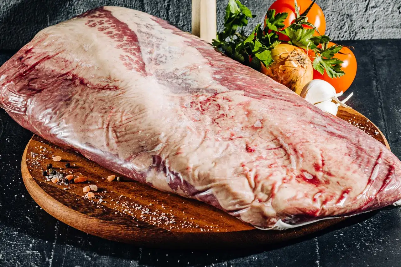 En stor bit oxbringa, redo f&ouml;r grillen, med salt, peppar, l&ouml;k, vitl&ouml;k och tomater som tillbeh&ouml;r.