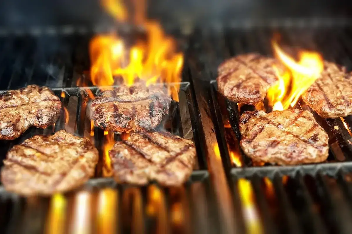 Grilla hamburgare över öppna lågor. Saftiga biffar får fina grillränder och doften sprider sig.