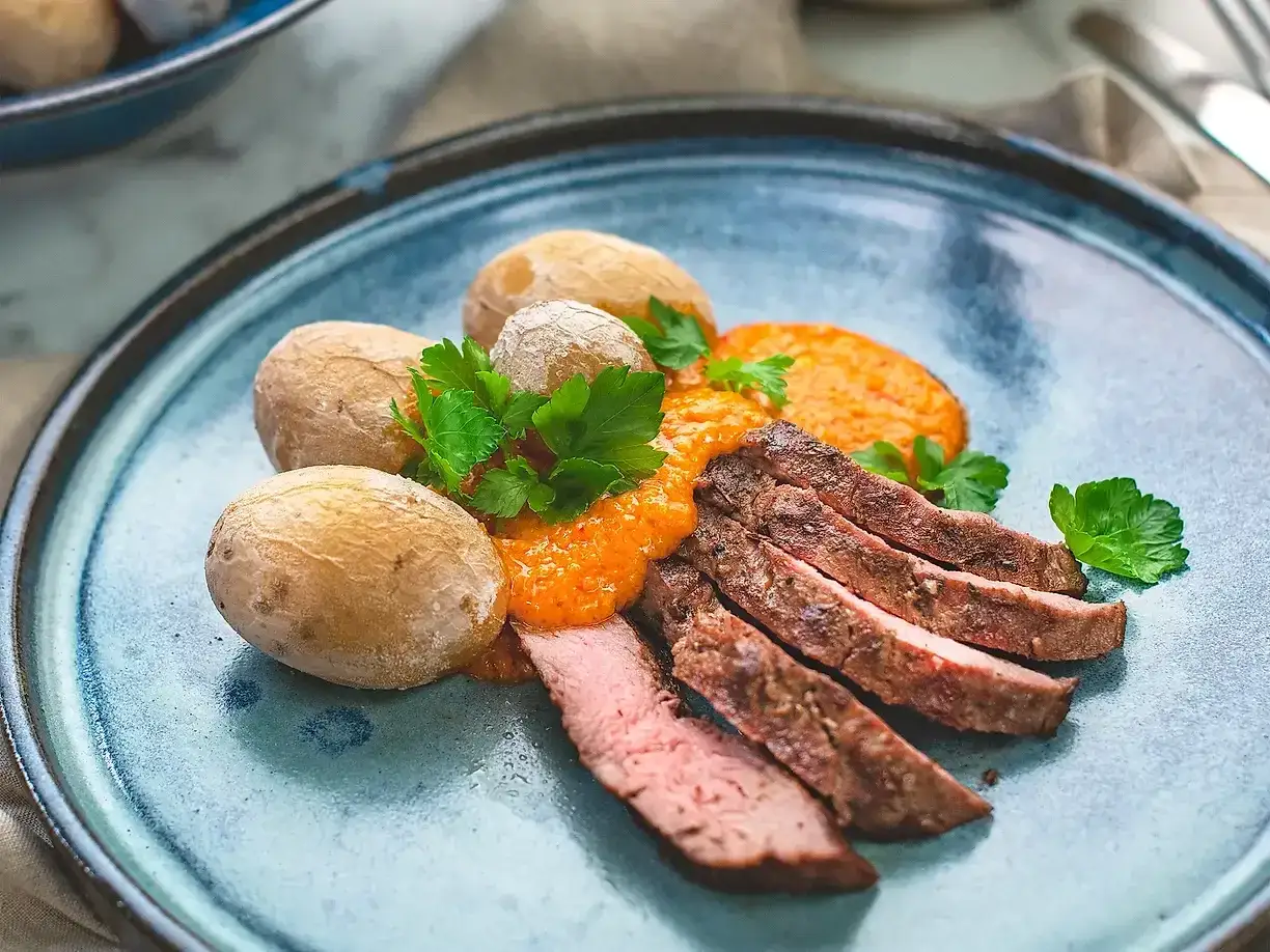 Skivat, saftigt k&ouml;tt fr&aring;n grilla pluma serveras med sm&aring;, salta potatisar och en smakrik s&aring;s.