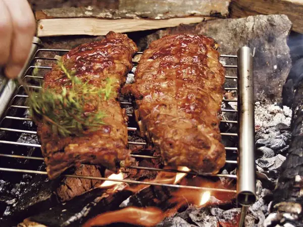 Två saftiga grillade spareribs på ett grillgaller över öppen eld. En kvist rosmarin läggs på för extra smak.